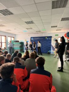 uczennice w czarnych fartuchach stoją przed publicznością na tle ścianki Zespołu Szkół w Bolechowie.